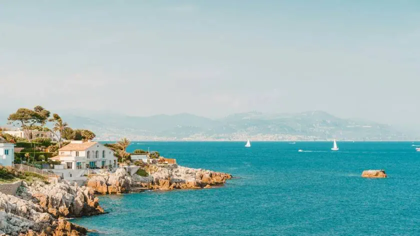 Plage méditerranéenne avec maisons et yachts, paysage côtier ensoleillé.