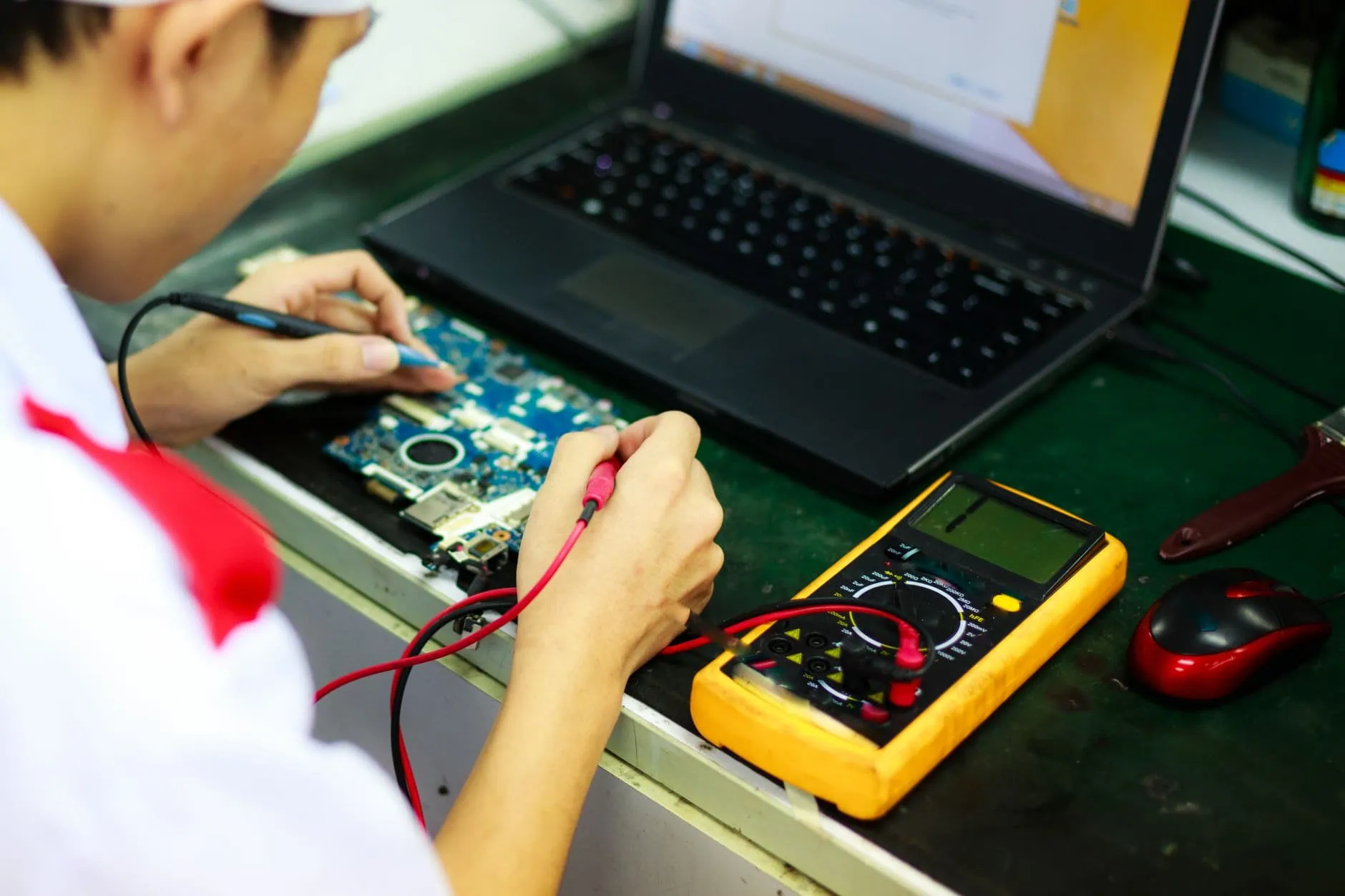 Comment savoir si votre Mac est obsolète (Guide 2026) 1 Technicien mesurant les composants d'un ordinateur portable au multimètre dans un atelier