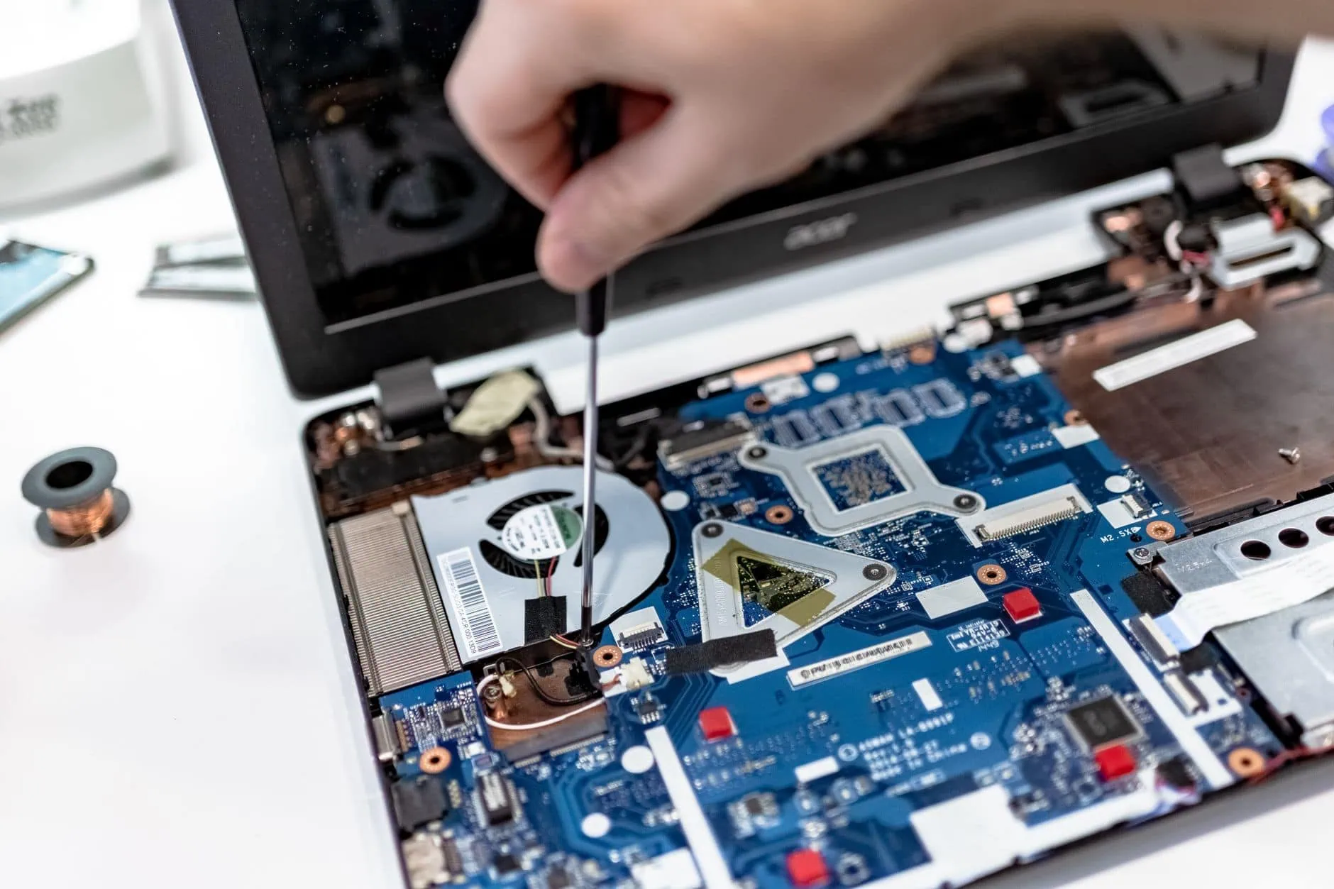 Comment savoir si votre Mac est obsolète (Guide 2026) 2 Main d'un technicien intervenant au tournevis sur la carte mère d'un ordinateur portable ancien